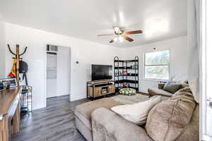 Living room featuring stacked washer and clothes dryer, a ceiling fan, and wood finished floors