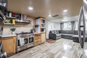 Kitchen with appliances with stainless steel finishes, wall chimney range hood, open floor plan, recessed lighting, and glass insert cabinets