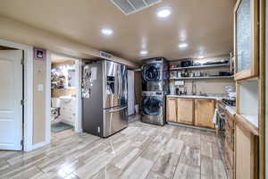 Kitchen with stacked washer and clothes dryer, appliances with stainless steel finishes, light countertops, open shelves, and recessed lighting