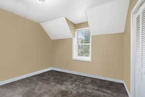 Bonus room with lofted ceiling and dark colored carpet
