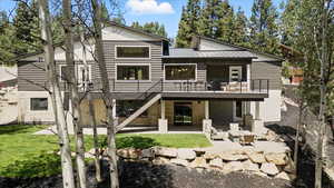 Rear view of house with a patio, a metal roof, a lawn, a wooden deck, and stairway