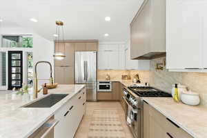 Kitchen with modern cabinets, premium appliances, recessed lighting, decorative light fixtures, and light stone counters