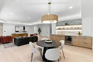 Dining room with beverage cooler, recessed lighting, light wood-style floors, bar, and a raised ceiling