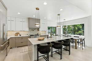 Kitchen with modern cabinets, decorative backsplash, light stone countertops, a kitchen island with sink, and recessed lighting