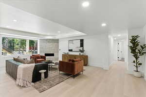 Living area featuring recessed lighting, light wood-style flooring, a stone fireplace, and a raised ceiling