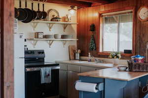 Kitchen featuring open shelves, stainless steel electric stove, freestanding refrigerator, light countertops, and wooden walls