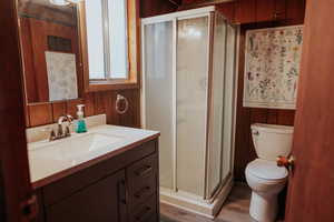 Bathroom featuring wooden walls, vanity, a stall shower, and wood finished floors