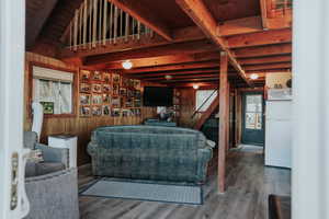 Living area with wood finished floors, healthy amount of natural light, wooden walls, wood ceiling, and stairway