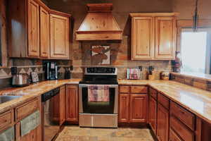 Kitchen featuring appliances with stainless steel finishes, custom exhaust hood, light stone finish floors, pendant lighting, and backsplash