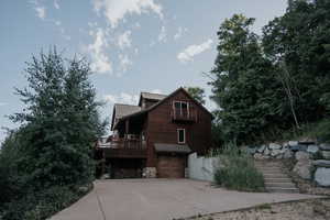 View of side of home featuring a balcony, an attached garage, driveway, stone siding, and a metal roof