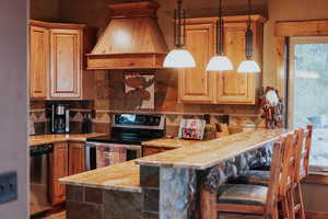 Kitchen featuring stainless steel appliances, premium range hood, tasteful backsplash, decorative light fixtures, and a peninsula
