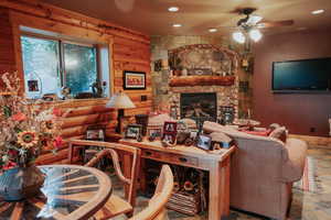 Living room with recessed lighting, a stone fireplace, a ceiling fan, and log walls