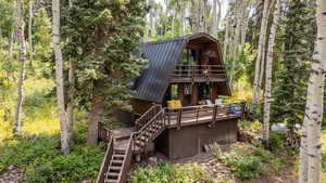 Rear view of house with a gambrel roof, stairs, a metal roof, and a view of trees