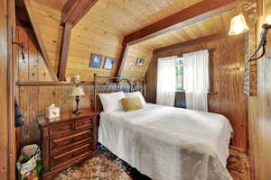 Bedroom with a wooden ceiling with exposed beams and wooden walls