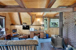 Carpeted bedroom featuring a wood stove, wooden ceiling, and wood walls