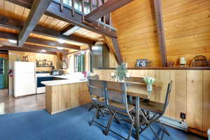 Kitchen with white appliances, a wood ceiling with exposed beams, a peninsula, baseboard heating, and wood walls