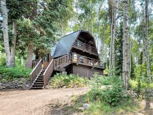 Rear view of house with a gambrel roof, a metal roof, stairway, and a wooded view