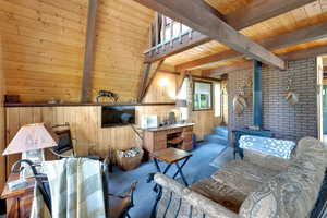 Living area with a wood stove, a wooden ceiling with exposed beams, carpet, and wood walls