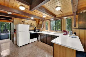 Kitchen featuring healthy amount of natural light, white appliances, wood walls, light countertops, and a wooden ceiling with exposed beams