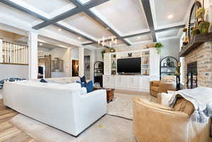 Living area with a brick fireplace, ornate columns, beamed ceiling, and coffered ceiling
