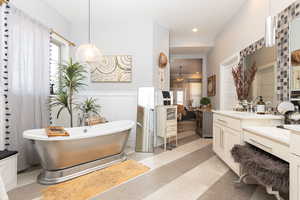 Full bathroom with a decorative wall, vanity, wainscoting, a freestanding bath, and tile patterned floors