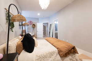 Carpeted bedroom featuring baseboards, an inviting chandelier, and connected bathroom