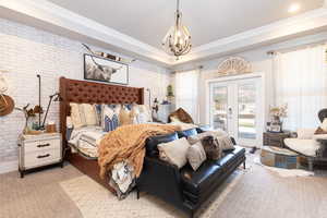 Bedroom with a notable chandelier, brick wall, crown molding, access to outside, and light carpet