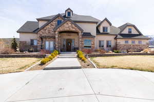 View of front of property featuring french doors, stucco siding, stone siding, and a front lawn