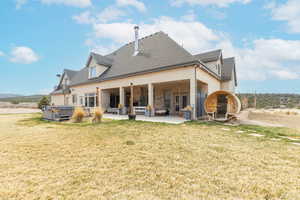 Rear view of property with a patio, a shingled roof, a hot tub, and a lawn