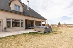 Rear view of property featuring a hot tub, a yard, a patio, stucco siding, and roof with shingles