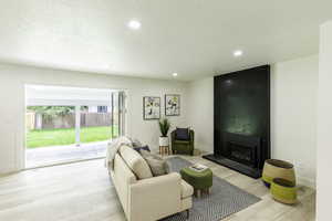 Living area featuring light wood-type flooring, a large fireplace, recessed lighting, and a textured ceiling