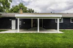 Rear view of house with a patio, a shingled roof, a lawn, and a chimney