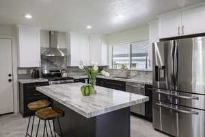 Kitchen featuring appliances with stainless steel finishes, wall chimney range hood, a kitchen bar, white cabinetry, and a textured ceiling