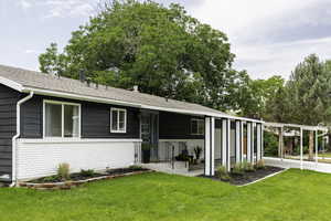 Rear view of property with a lawn, an attached carport, a shingled roof, and brick siding