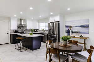 Kitchen with stainless steel appliances, a center island, wall chimney exhaust hood, white cabinetry, and recessed lighting