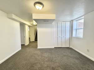 Additional living space with a textured ceiling, dark carpet, and stairway