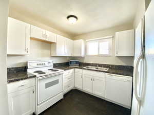 Kitchen featuring white appliances, white cabinets, dark wood-style floors, and dark stone counters