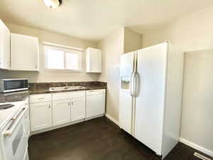 Kitchen with white appliances, white cabinetry, and dark wood-type flooring