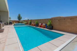 View of pool featuring a pool with connected hot tub, a fenced backyard, grilling area, and a patio area