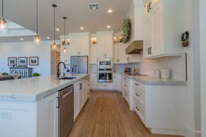 Kitchen featuring appliances with stainless steel finishes, white cabinetry, light wood-style flooring, tasteful backsplash, and recessed lighting