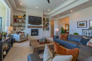 Living room featuring built in shelves, a brick fireplace, recessed lighting, light colored carpet, and a tray ceiling