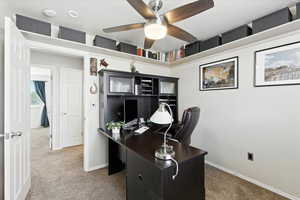 Carpeted office space featuring a ceiling fan and baseboards