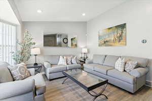 Living room with vaulted ceiling, wood finished floors, and recessed lighting