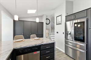 Kitchen featuring stainless steel appliances, lofted ceiling, light stone counters, decorative light fixtures, and light wood-style floors