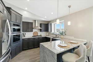 Kitchen with a peninsula, appliances with stainless steel finishes, light stone countertops, vaulted ceiling, and light wood-style floors