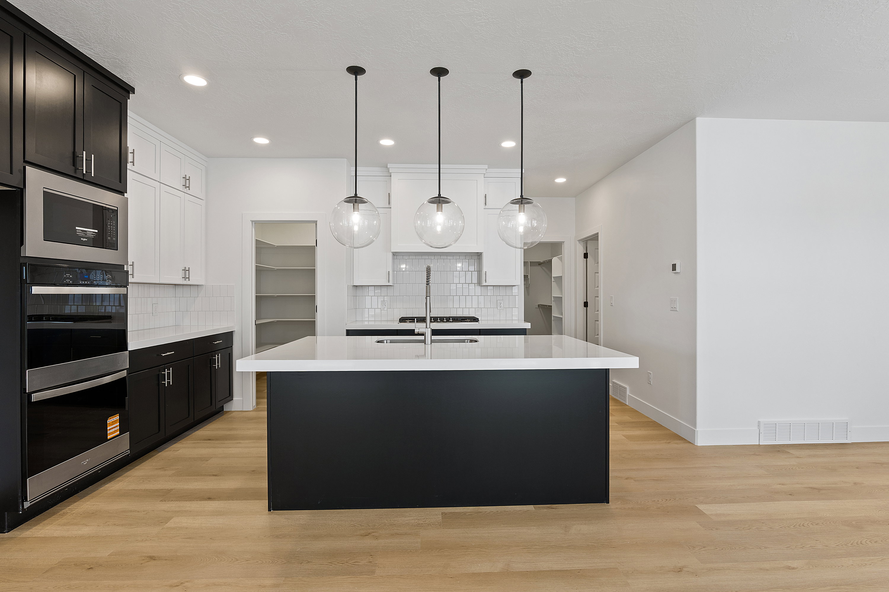 Kitchen with tasteful backsplash, light countertops, a kitchen island with sink, double oven, and light wood-style floors