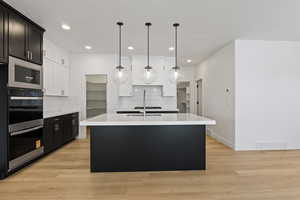 Kitchen with tasteful backsplash, light countertops, a kitchen island with sink, double oven, and light wood-style floors