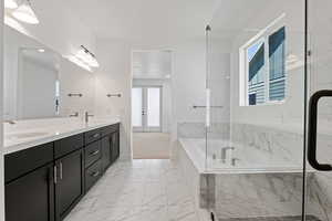 Bathroom featuring french doors, double vanity, a bath, and healthy amount of natural light