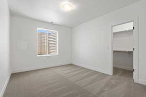 Unfurnished bedroom featuring carpet flooring, a walk in closet, and a textured ceiling