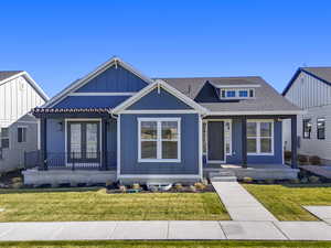 View of front of property with a front yard, covered porch, roof with shingles, and board and batten siding